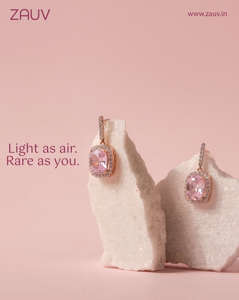 A close-up aesthetic shot of rose gold earrings resting on raw white stone fragments against a soft pink backdrop.