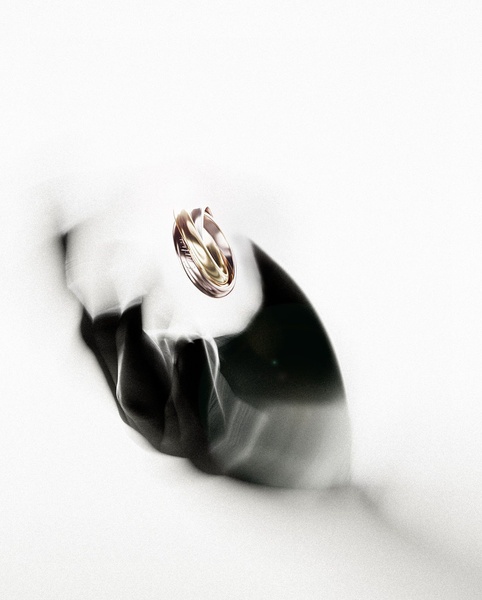 A high-contrast, artistic studio shot of a triple-band ring suspended in mid-air above a dark, shadowed hand silhouette against a stark white background.