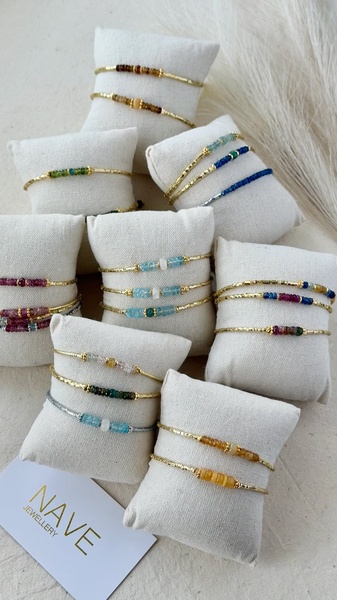 A high-quality 9:16 vertical grid layout displaying multiple colorful bead bracelets on neutral textured pillows, emphasizing brand elegance.