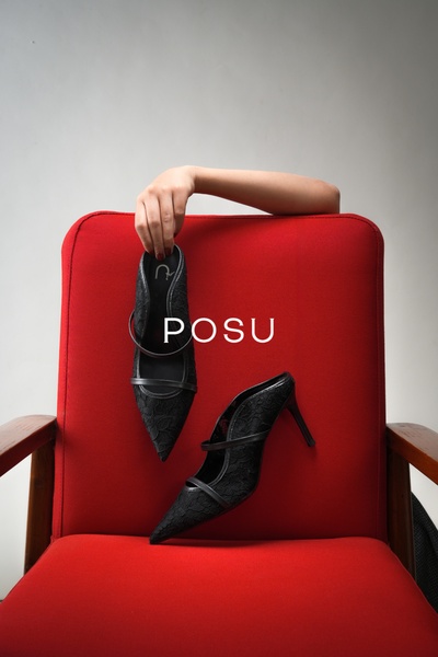 A high-contrast advertisement featuring black lace heels held against a vivid red chair, utilizing negative space for a premium brand focus.