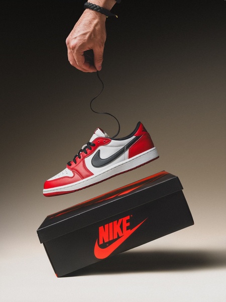 A minimalist studio shot featuring a running shoe suspended in mid-air, held by a thin string against a clean background with the product box.