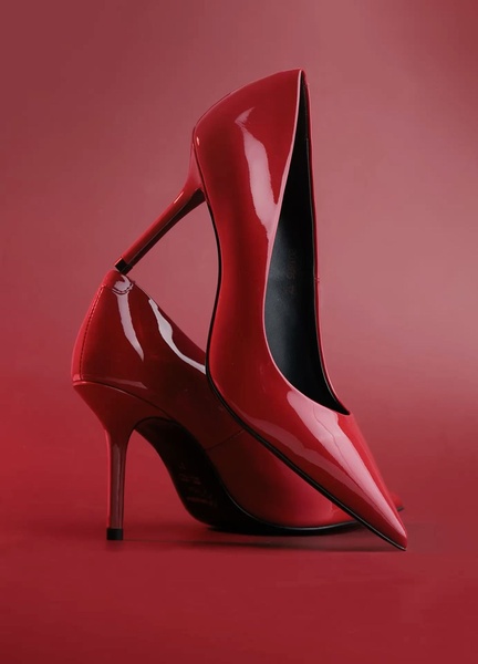 A high-fashion, minimalist product showcase featuring two glossy red stiletto pumps against a matching red background to emphasize shape and material.