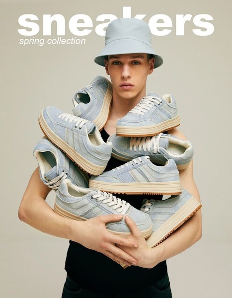 A clean, studio-lit portrait of a model holding a stack of identical sneakers, emphasizing the product range and spring aesthetic.