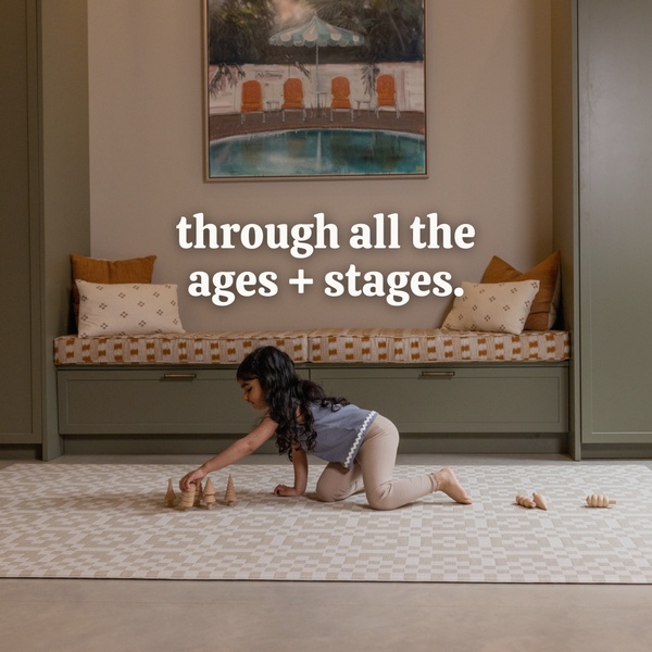 A clean, lifestyle-oriented image of a child playing with wooden toys on a minimalist patterned play mat in a cozy, neutral-toned living space.