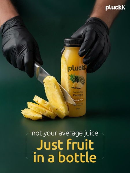 A high-quality studio shot featuring a bottle of pineapple juice alongside sliced fresh fruit, held by gloved hands to emphasize cleanliness and product quality.