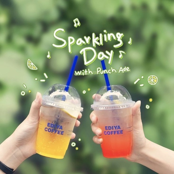 A bright, lifestyle-focused ad showing two people toasting with colorful fruit-based beverages against a natural, blurred green background.