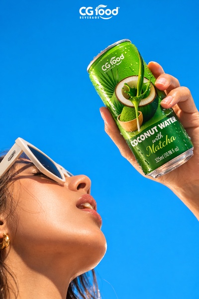 A vibrant, outdoor lifestyle shot featuring a hand holding a chilled can of coconut water with matcha against a bright blue sky.
