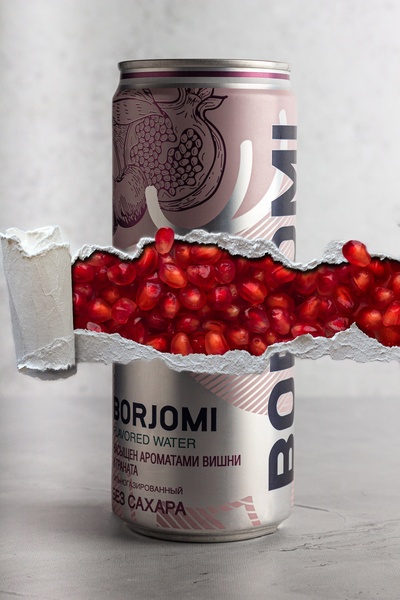 A striking product shot showing a can of pomegranate flavored water behind a realistic paper-tear effect, revealing fresh pomegranate arils inside.