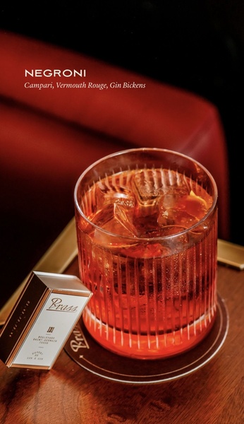 A high-end, editorial-style product shot of a Negroni in a crystal glass on a dark, polished wood surface, paired with a subtle brand card.