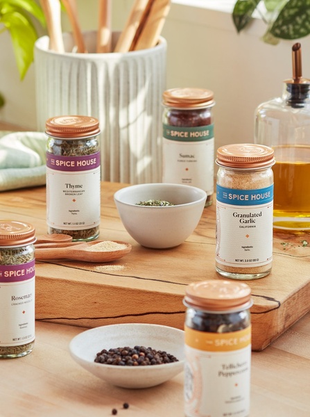A high-quality product hero shot showcasing premium spices in glass jars on a wooden kitchen surface with soft natural lighting.