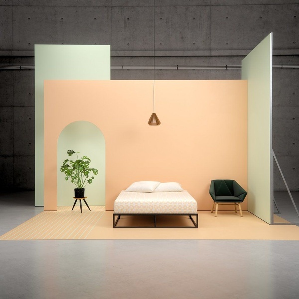 A clean, studio-lit mattress product shot using a split-level wall design, pastel color blocking, and purposeful negative space to isolate the furniture.