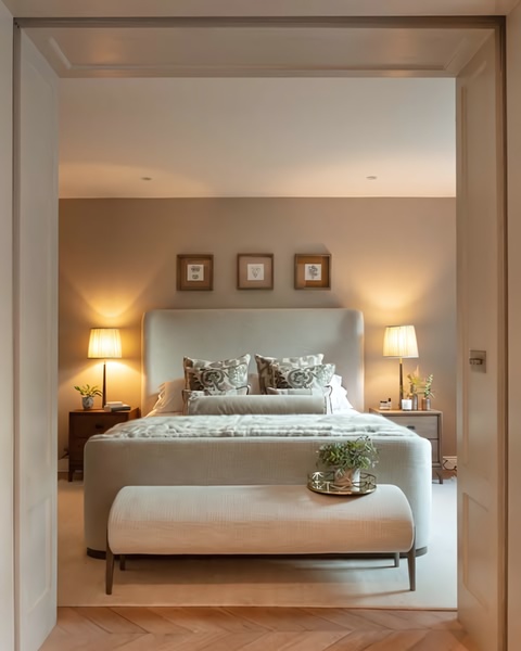 A symmetrically composed interior shot of a neutral-toned upholstered bed centered in a warm, inviting bedroom space.