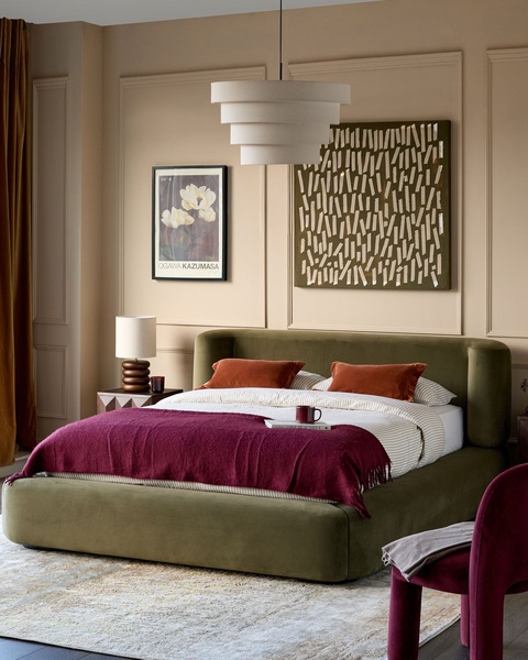 A high-end editorial shot featuring an olive green upholstered bed in a neutral, sophisticated room setting with layered textures.