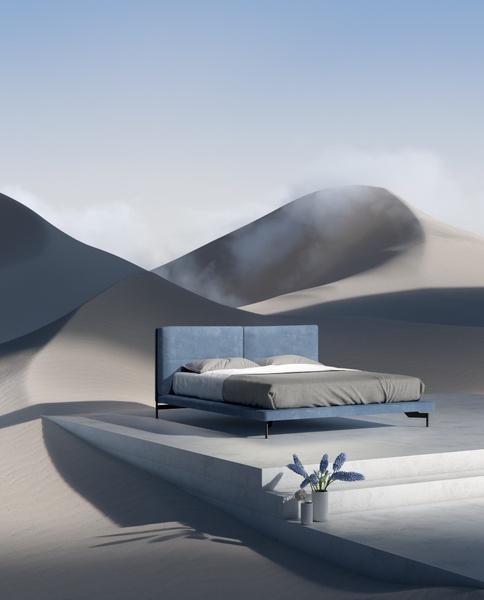 A high-end blue upholstered bed is centered on a concrete platform set within a surreal, minimalist desert landscape under soft light.