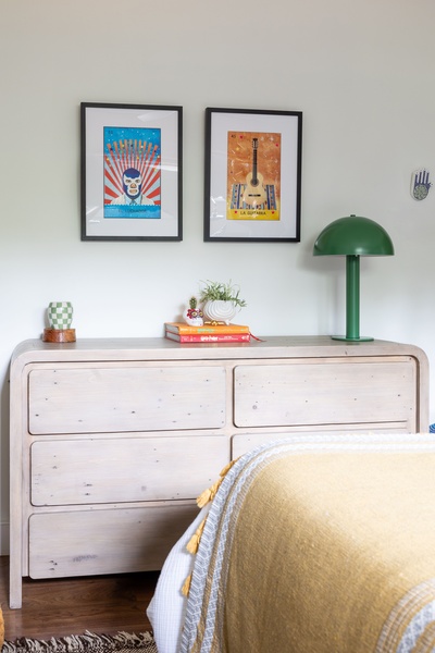 A high-quality lifestyle shot featuring a light wood grain six-drawer dresser styled with art and a lamp in a warm bedroom setting.