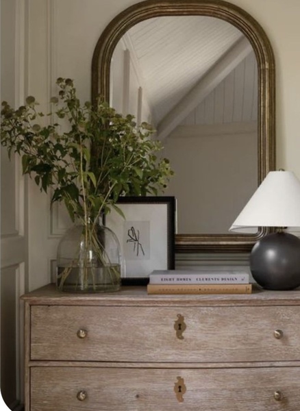A refined lifestyle shot of a wooden dresser styled with a mirror, lamp, and greenery, emphasizing a calm and premium atmosphere.