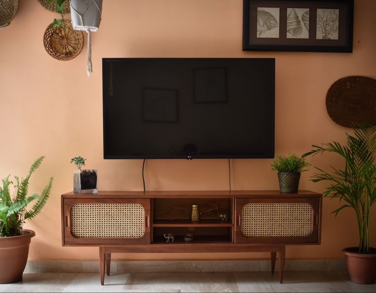 A high-quality 5:4 static shot featuring a rattan-paneled media console centered under a television, surrounded by warm ambient decor.