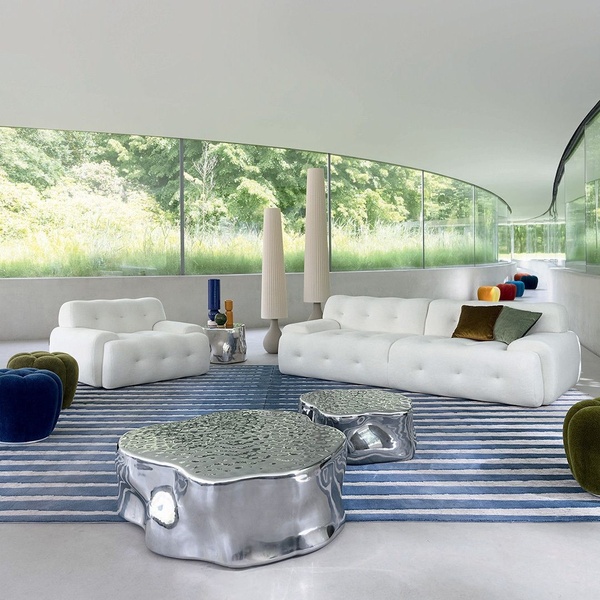 A high-end furniture setup featuring a white button-tufted sofa, matching armchair, and metallic coffee tables inside a curved architectural space.