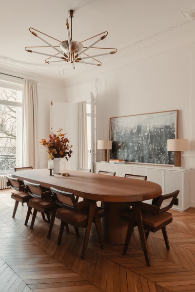 A high-end, aspirational dining room scene featuring a wooden oval table and rattan chairs, captured in a bright, neutral aesthetic.