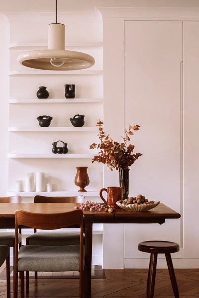 A high-end lifestyle shot of a modern dining space featuring neutral-toned ceramic vases on tiered shelves and a wooden table.