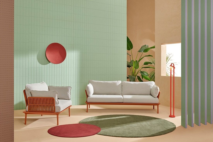 A high-end furniture ad featuring a sofa and armchair in a color-blocked studio setting, utilizing negative space and geometric rugs.