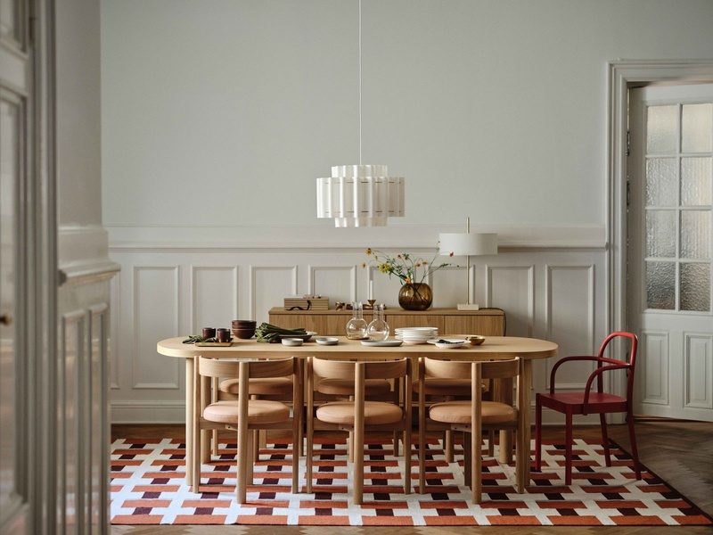 A high-end dining table set in a neutral-toned room with warm lighting, featuring modern wooden chairs and an eye-catching geometric patterned rug.
