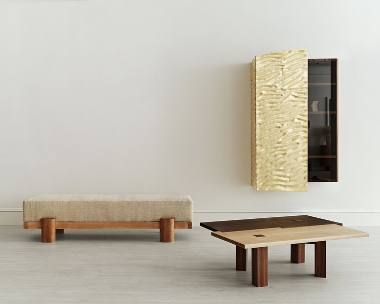 A high-end furniture ad featuring a minimalist bench, a floating gold-textured cabinet, and a multi-toned wooden coffee table in a studio setting.