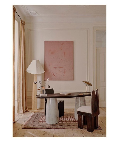 A sophisticated, high-end studio shot of a dark oval dining table set in a warm, neutral-toned room with artistic accessories.