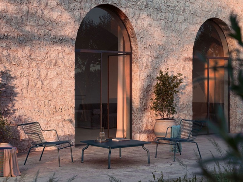 A high-end lifestyle shot of outdoor lounge chairs and a matching table on a stone patio during sunset.