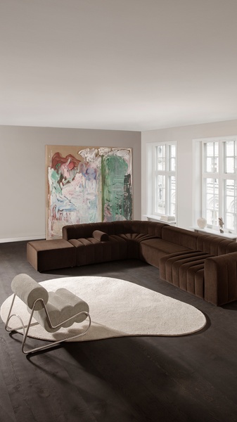 A high-end, clean-lined photograph featuring a deep brown sectional sofa and a sculptural lounge chair in a bright, modern living space.
