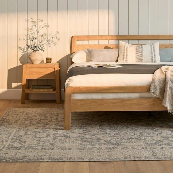 A high-quality lifestyle shot of a natural wood bed frame featuring soft, golden-hour lighting that emphasizes texture and serenity.