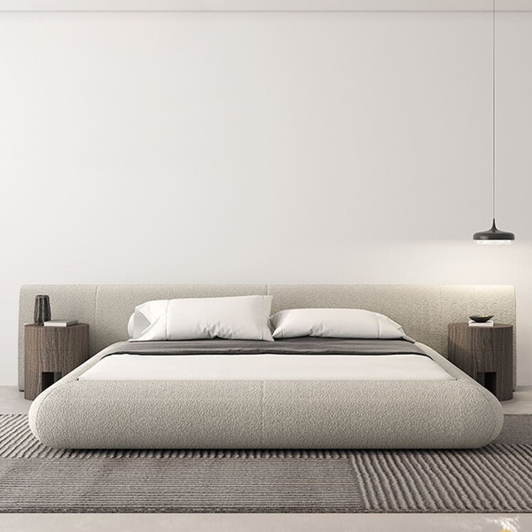 A centered, symmetrical product hero shot of a modern upholstered bed against a clean white wall, featuring warm lighting and textured textiles.