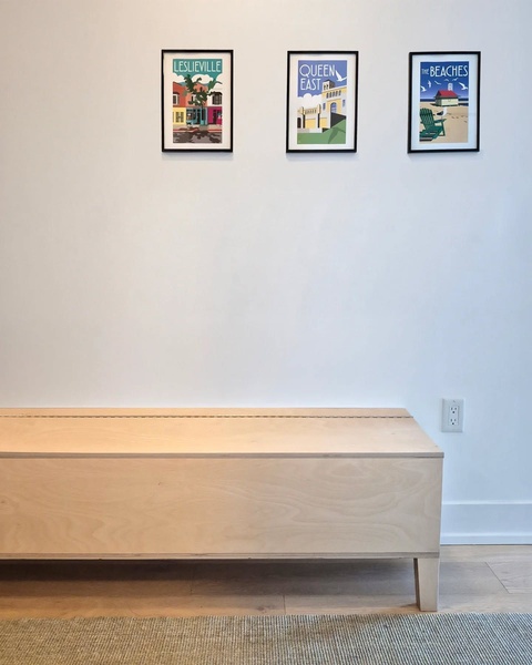 A clean, eye-level shot of a handcrafted wooden bench positioned against a plain wall with framed local art above.