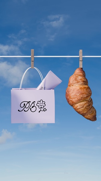 A high-concept aesthetic ad showing a skincare tube in a shopping bag suspended on a clothesline next to a croissant against a blue sky.