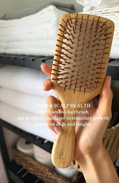 A close-up, hand-held shot of a bamboo hairbrush featuring direct, benefit-focused text overlaying the product.