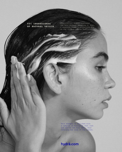 A high-contrast, black and white portrait featuring a model applying a hair treatment product, focusing on ingredient transparency and texture.