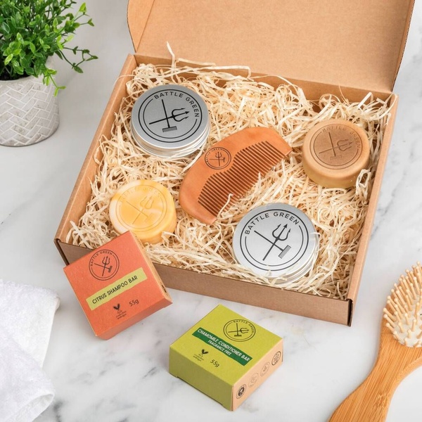 A flat-lay photograph of a Shampoo Bar and Conditioner Bar kit in a cardboard box, surrounded by wood shavings and natural accessories.
