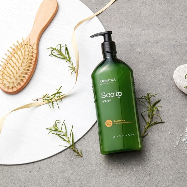 A clean, high-quality product hero shot for scalp scaling shampoo featuring rosemary sprigs and wooden hair care accessories on a neutral stone background.