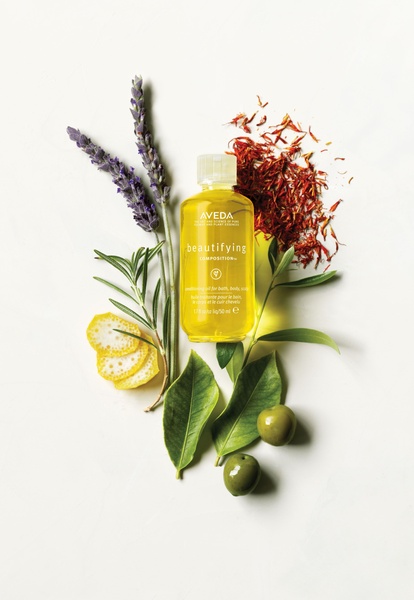 A high-quality flat lay product shot of a conditioning oil surrounded by its organic ingredients like lavender and olives on a white background.