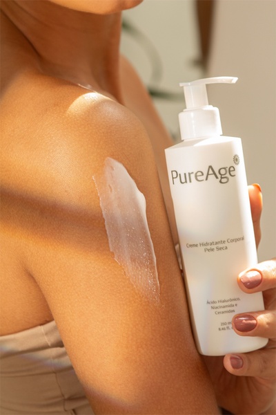 A close-up photograph featuring a person applying a white body moisturizer to their skin, highlighting the product's texture and branding.