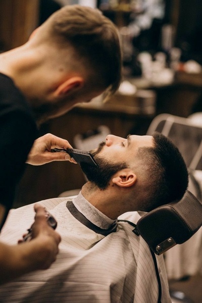 A high-quality, cinematic shot showing a barber carefully grooming a client's beard, focusing on precision and professional service.