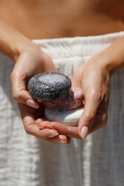 A close-up shot of hands holding three distinct shampoo bars, emphasizing the product's texture and natural origin.