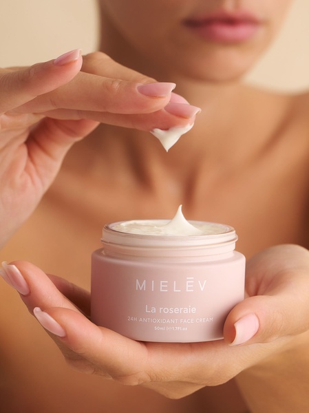 A close-up aesthetic shot of a jar of antioxidant face cream being held, showing a small dollop of the product on a fingertip to emphasize texture and consistency.