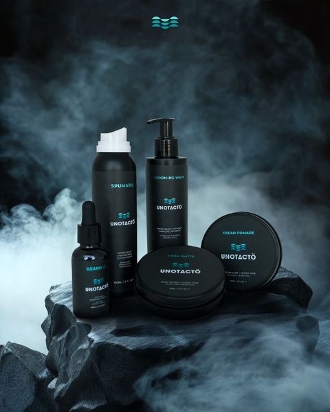 A high-end, studio-lit display of a grooming product collection resting on a dark rock formation amidst atmospheric smoke.