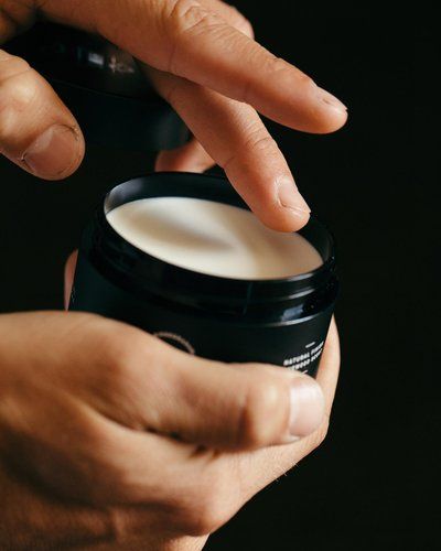 A close-up shot of a hand dipping a finger into a jar of hair pomade, highlighting the texture and quality of the product.