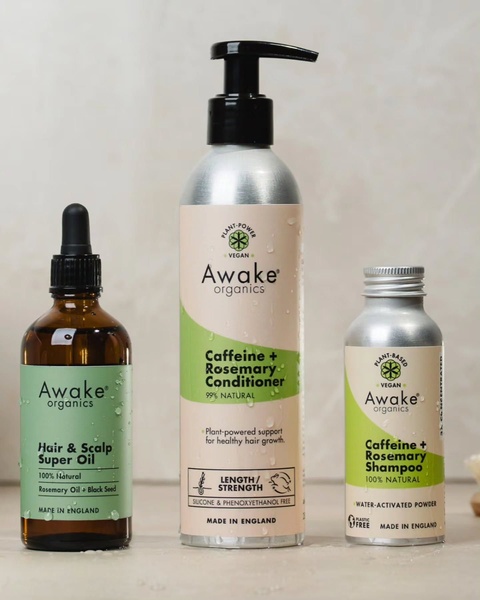 A high-quality product hero shot featuring three hair care bottles—a hair oil, a conditioner, and a powdered shampoo—arranged on a neutral surface.