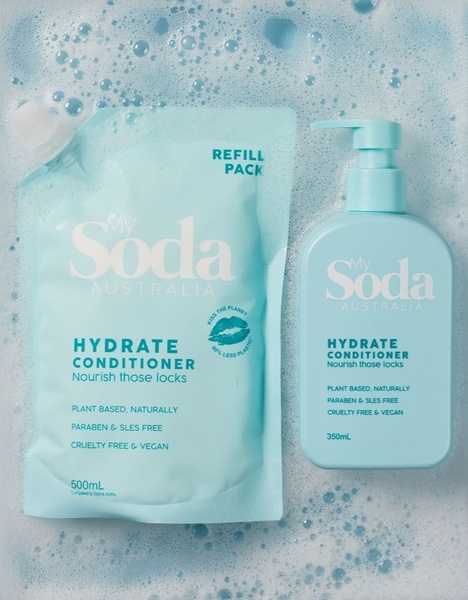 A clean, eye-level shot showing a conditioner bottle and refill pouch placed on a watery, soap-bubbly surface, highlighting the product as the hero.