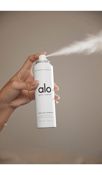 A high-quality studio shot of a hand holding a Dry Shampoo bottle while it is being sprayed, set against a neutral background.