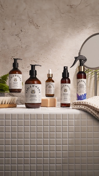This creative showcases a full line of hair care bottles arranged on a tiled surface with professional studio lighting and clean, high-end aesthetics.