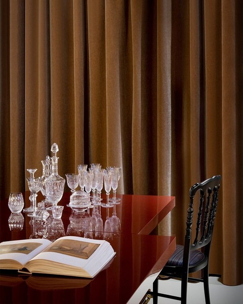A high-end, sophisticated display of fine crystal glassware set on a deep red table against rich, dark brown velvet curtains.